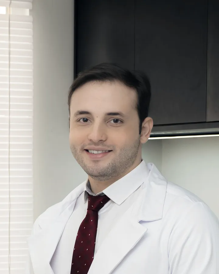 Dr. Daniel Ferraro in a white coat and red tie, standing in a consult room