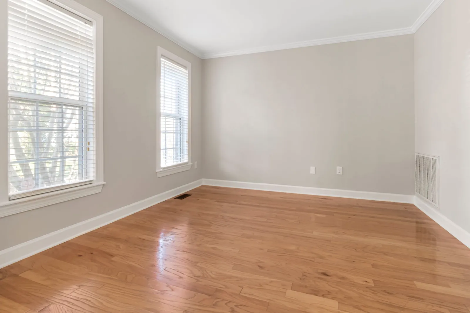 An empty front room with tall windows, crown molding and oak floors
